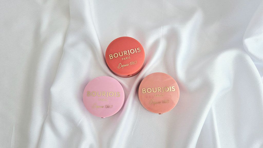 Blushs Bourjois Little Round Pot Blush posés sur un tissu blanc avec les teintes Rose Tendresse, Rose coup de foudre et Rouge Ravissant