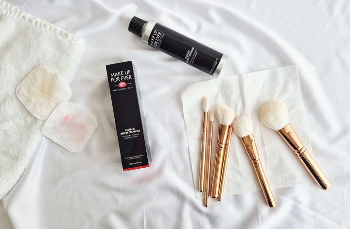 Vue de dessus montrant le nettoyant MUFE, des pinceaux de maquillage posés sur un mouchoir et deux cotons sales avec des résidus de maquillage colorés.