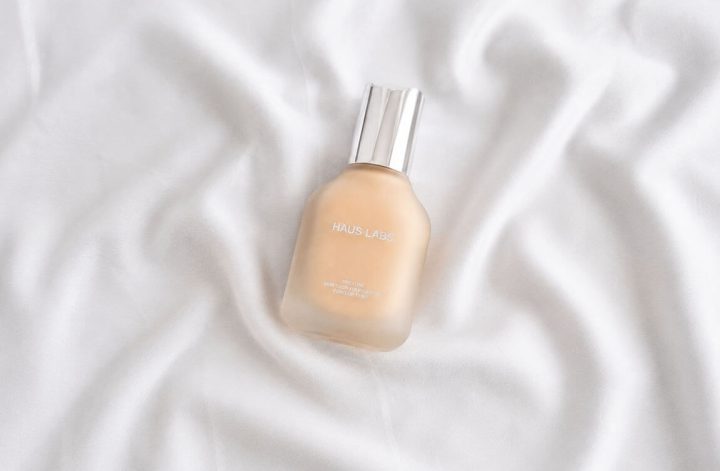 Flacon en verre dépoli du fond de teint Triclone Skin Tech Foundation de Haus Labs sur un tissu blanc satiné.