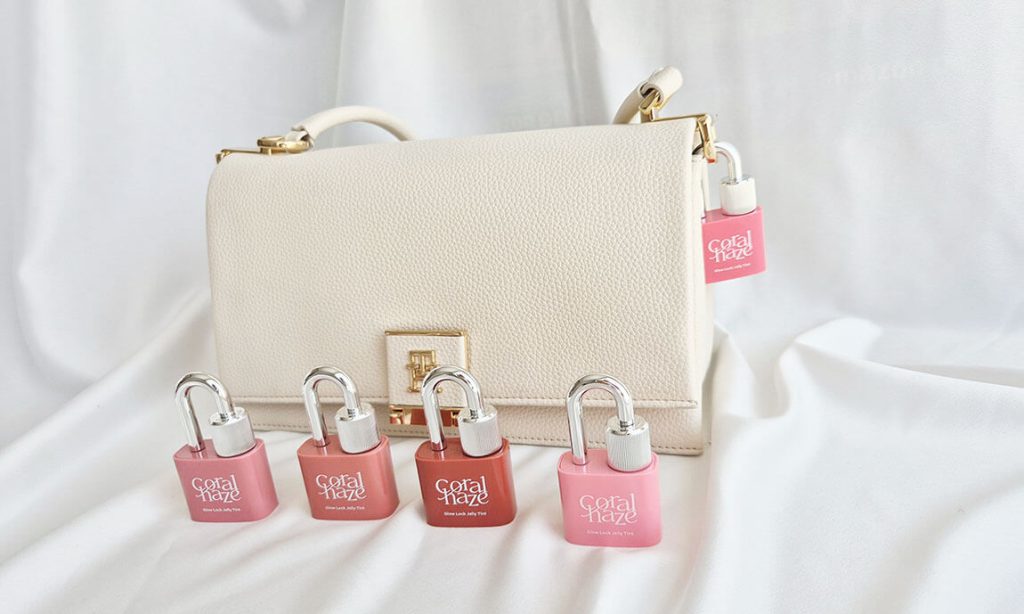 Packaging des Glow Lock Jelly Tint Coralhaze devant un sac à main blanc.