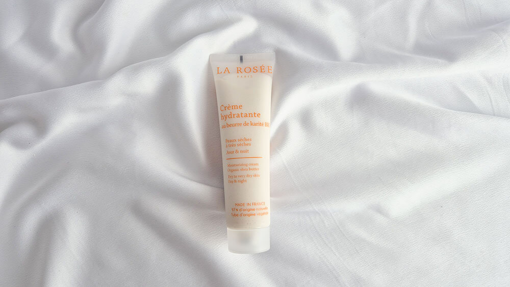 Tube de crème hydratante très riche au beurre de karité bio La Rosée posé sur un tissu blanc.