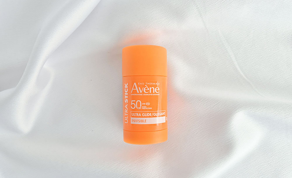 Le stick solaire Ultra Stick Invisible SPF 50 d'Avène posé sur un fond de tissu blanc satiné.