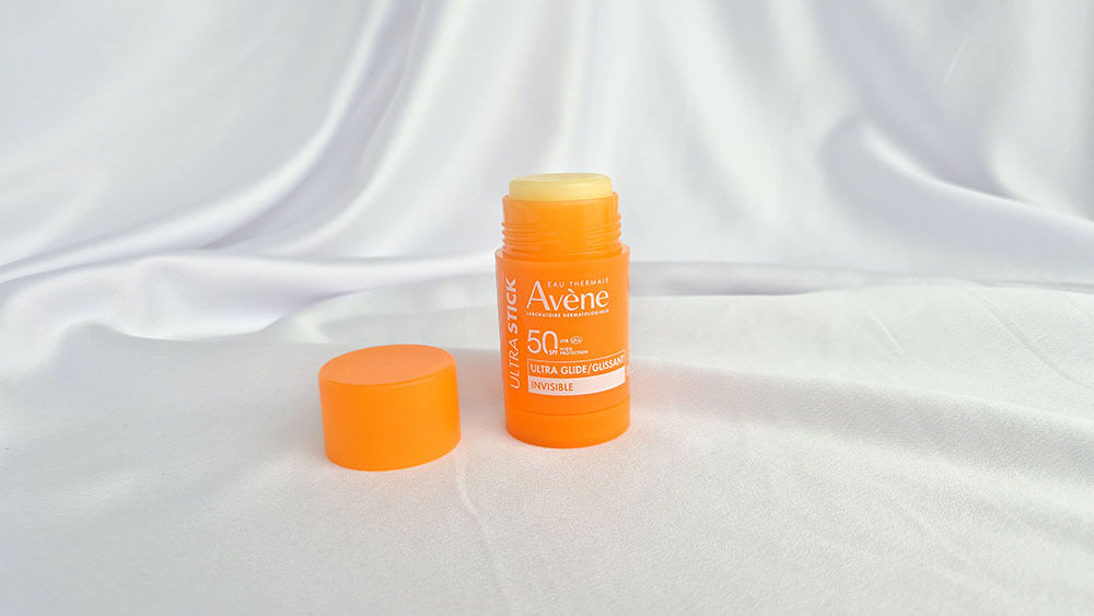 Tube orange de l'Ultra Stick Invisible SPF 50 d’Avène ouvert avec son bouchon posé à côté.