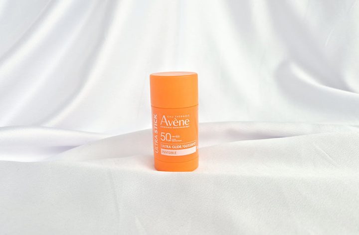 Stick solaire Ultra Stick Invisible SPF 50 d'Avène posé debout sur du tissu satiné blanc.